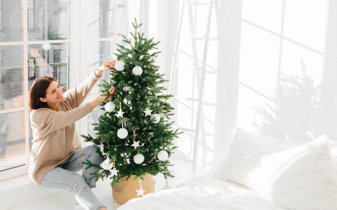 positive-young-female-poses-near-big-window-christmastree